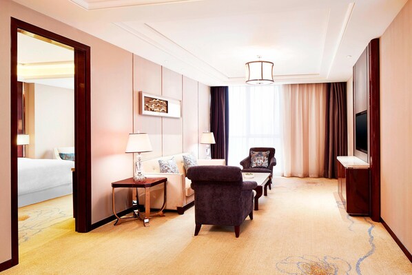 Une chambre d’hôtel comprenant un lit, un canapé, une chaise, une petite table, une lampe, un téléviseur et un grand miroir.