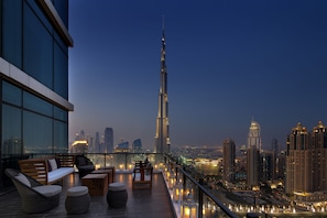 Una terraza en la azotea con vistas al Burj Khalifa, mobiliario moderno y un paisaje urbano al atardecer.