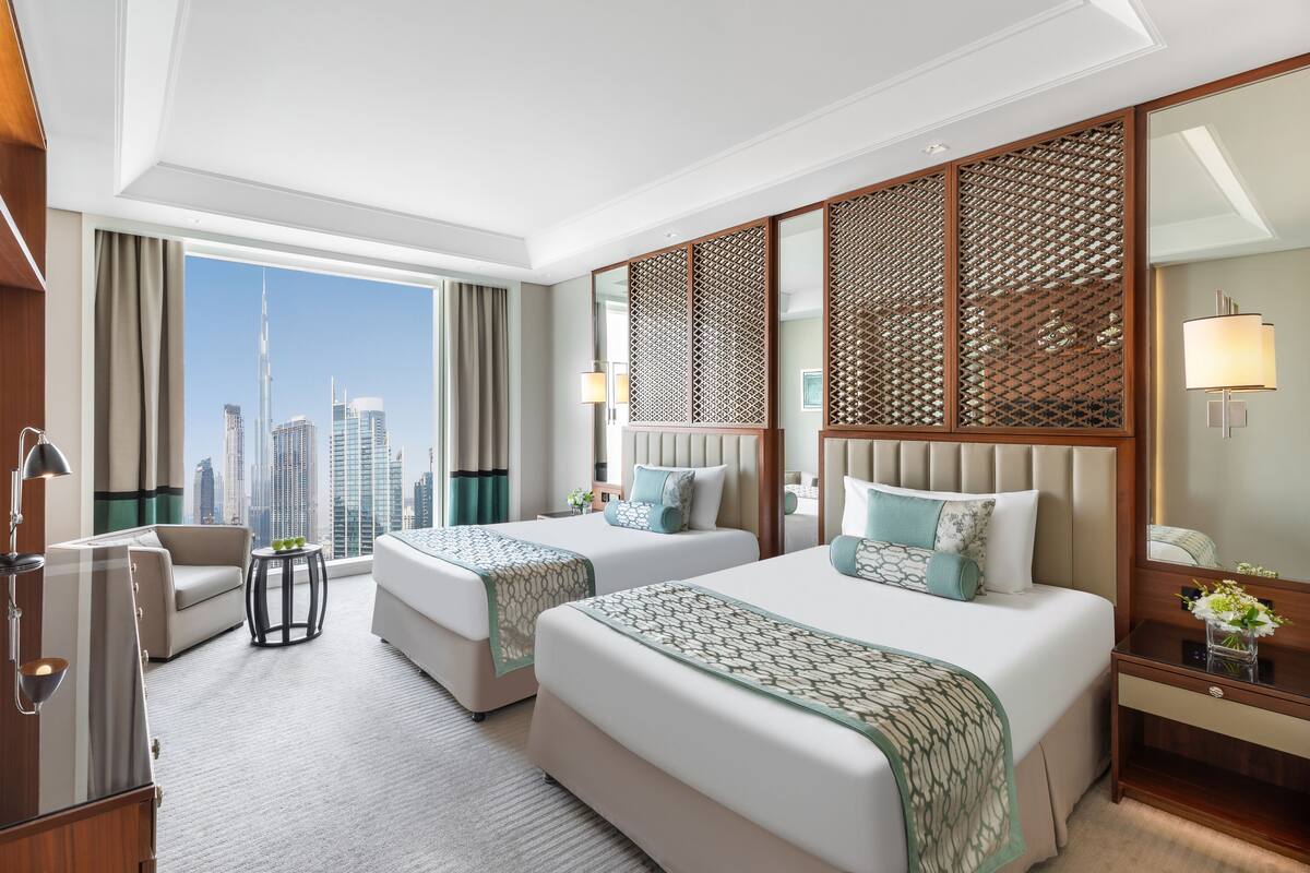 A hotel room with two beds, a sofa, a desk, and a view of the city skyline.