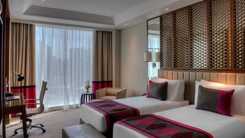 Ein Hotelzimmer mit zwei Betten, einem Schreibtisch, einem Stuhl und einem großen Fenster mit Vorhängen.