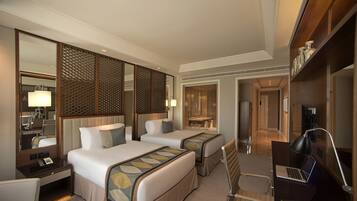 A hotel room with two beds, a desk with a lamp, a laptop, and a mirror.