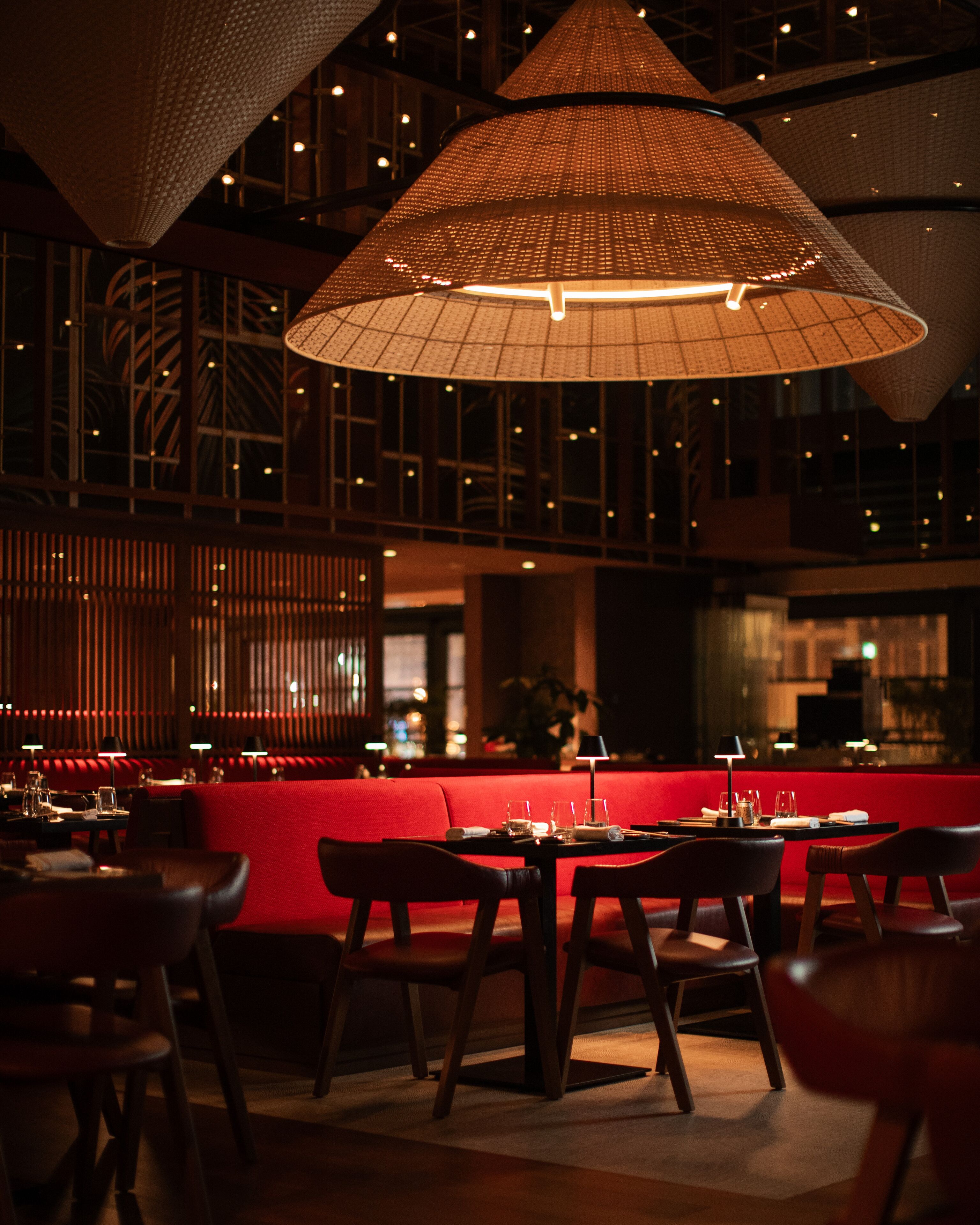 Un ristorante con sedute rosse, un'area bar e ampie lampade intrecciate.