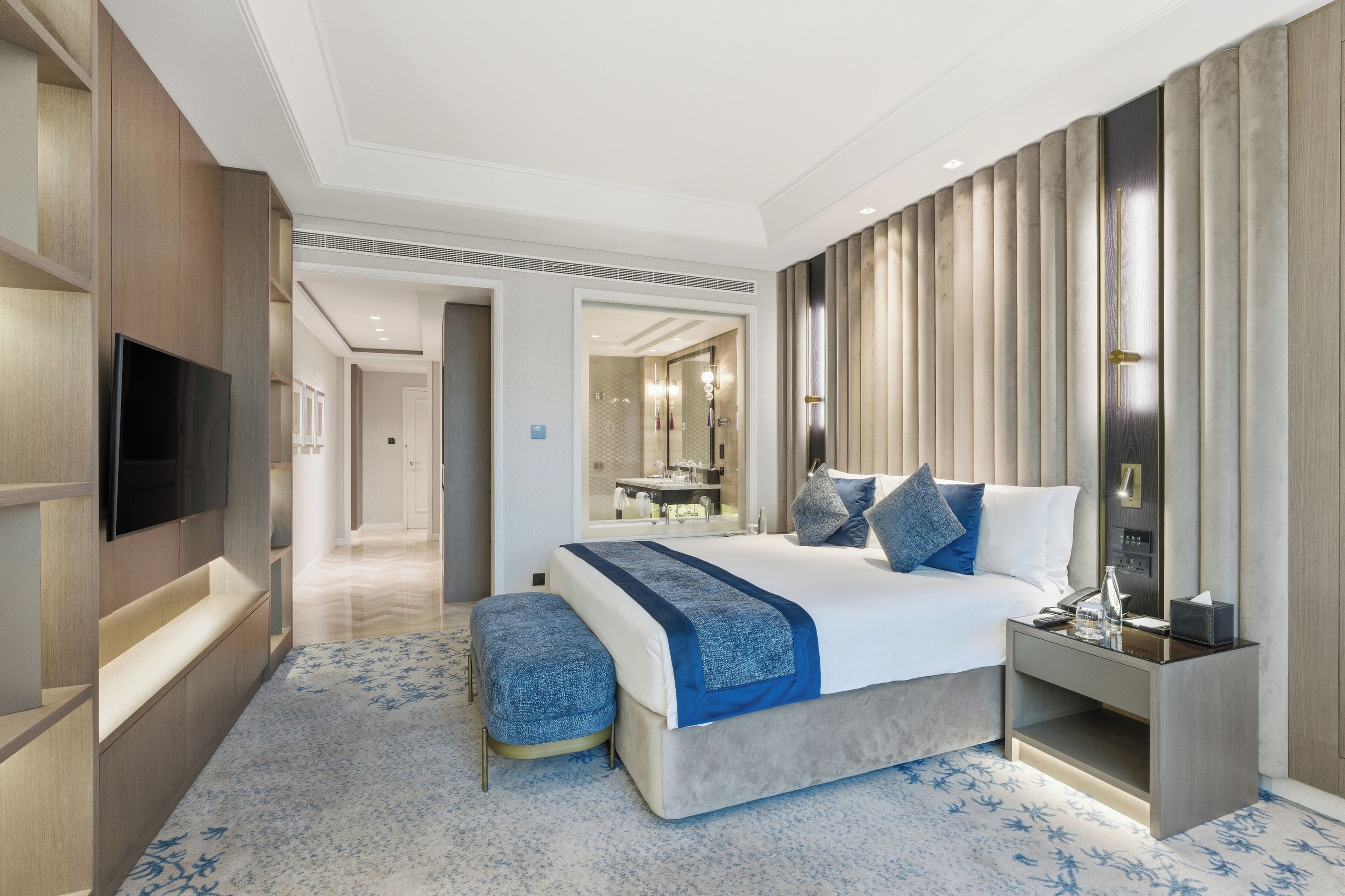 A modern hotel room with a large bed, a flat-screen TV, a bedside table, and a bathroom visible through an open door.