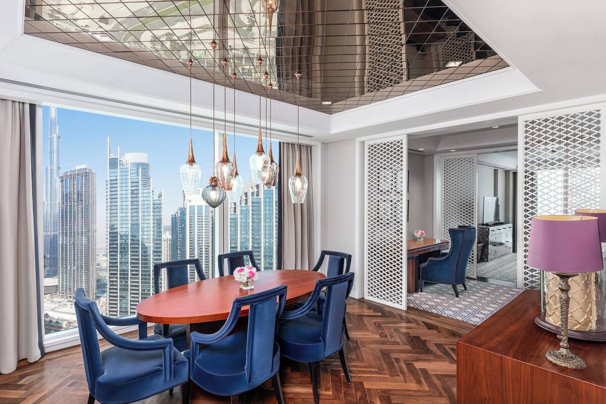 A modern dining area with a wooden table and blue chairs, large windows with a city view, and a decorative hanging light fixture.
