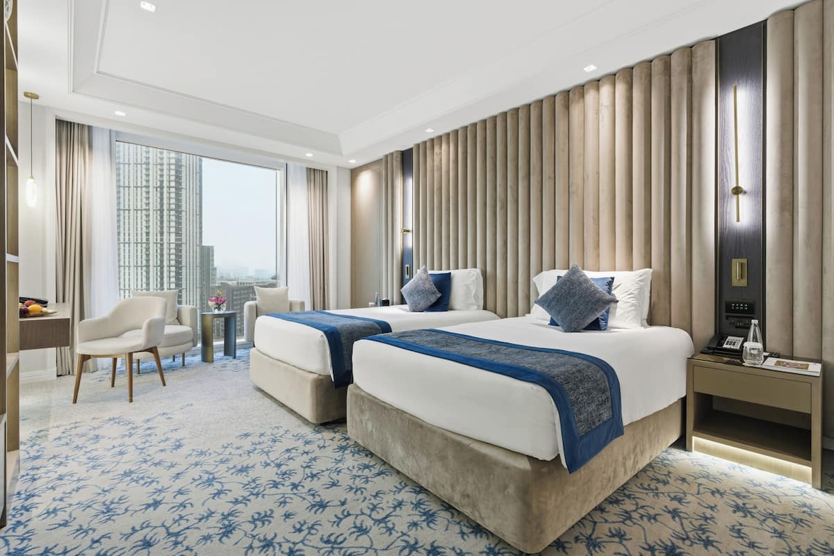 A hotel room with two beds, a desk, a chair, a small table, and a view of the city.