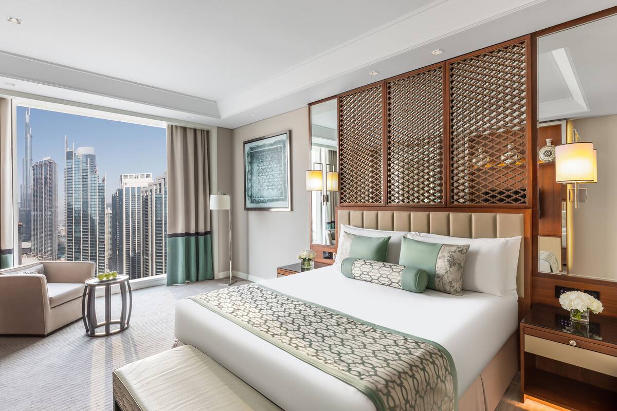 A hotel room with a large bed, a view of the cityscape, a seating area, and a decorative partition.