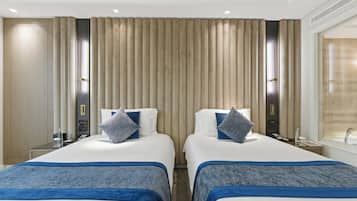 A hotel room with two beds, a minibar, a desk with a phone, and a bathroom with a sink and mirror.