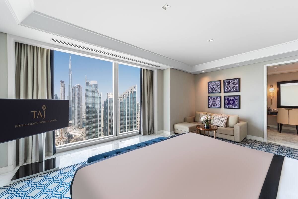 A modern hotel room with a large bed, a sofa, a TV, and a city view.