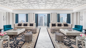 Un hall d’hôtel luxueux, à l’agencement symétrique, comprenant deux canapés placés face à face, un tapis central et une vue sur le paysage urbain à travers de grandes fenêtres.