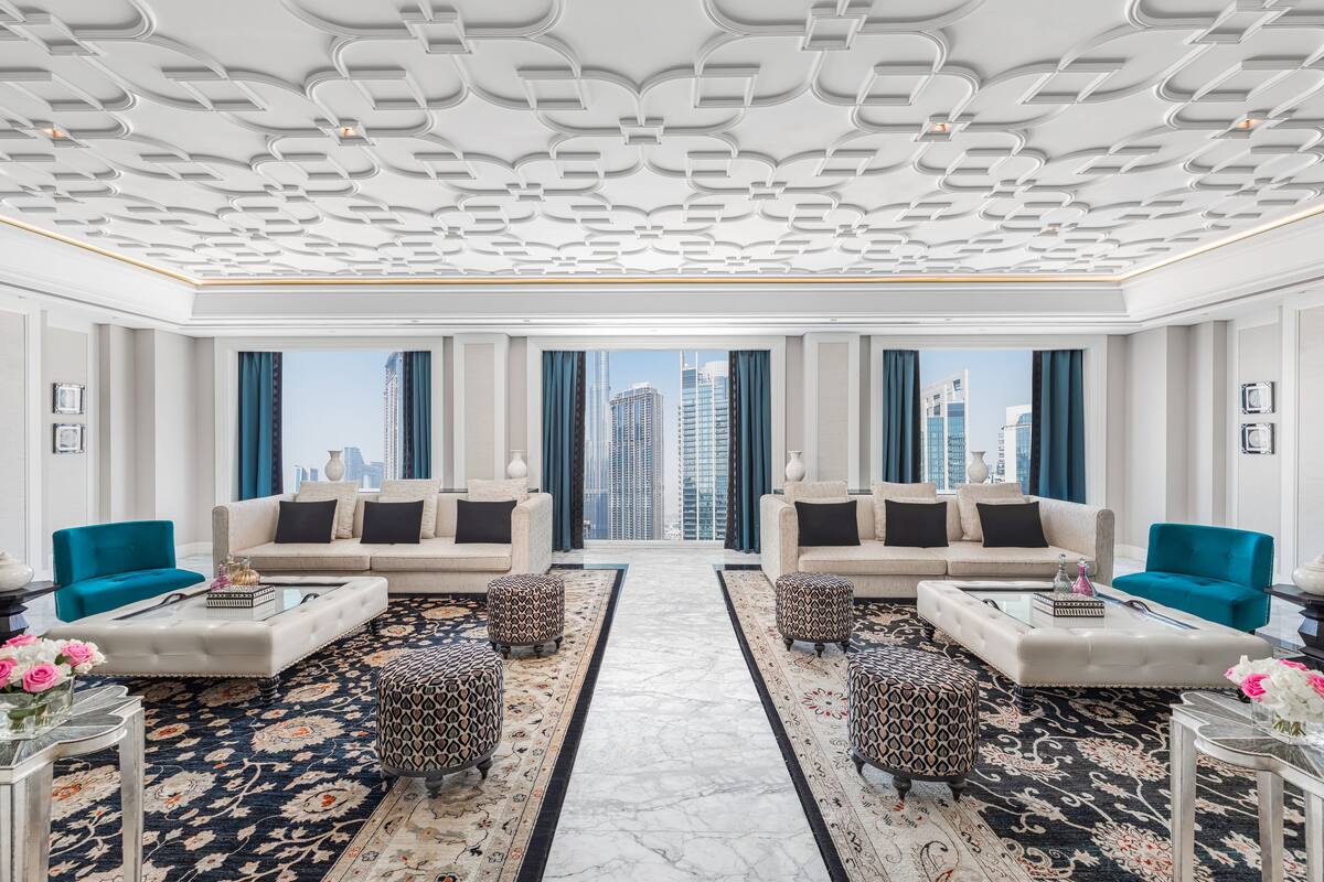A luxurious hotel lobby with a symmetrical layout, featuring two sofas facing each other, a central rug, and a view of the cityscape through large windows.