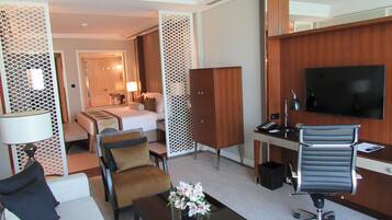 Habitación de hotel con cama, escritorio, televisor, sofá y mesa de centro con flores.