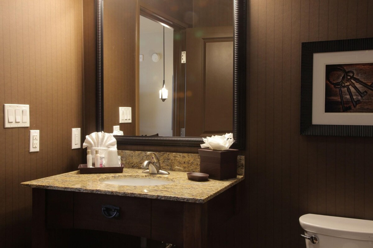A bathroom with a granite countertop sink, a mirror, a toilet, and a framed picture on the wall.