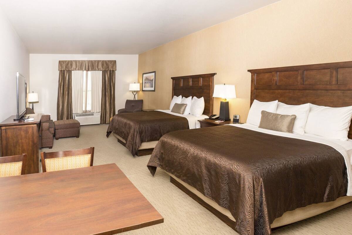 A hotel room with two beds, a desk, a chair, a TV, and a window with curtains.