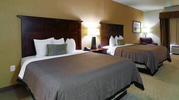 Una habitación de hotel con dos camas, una mesita de noche con lámpara, una silla y una ventana con cortinas.
