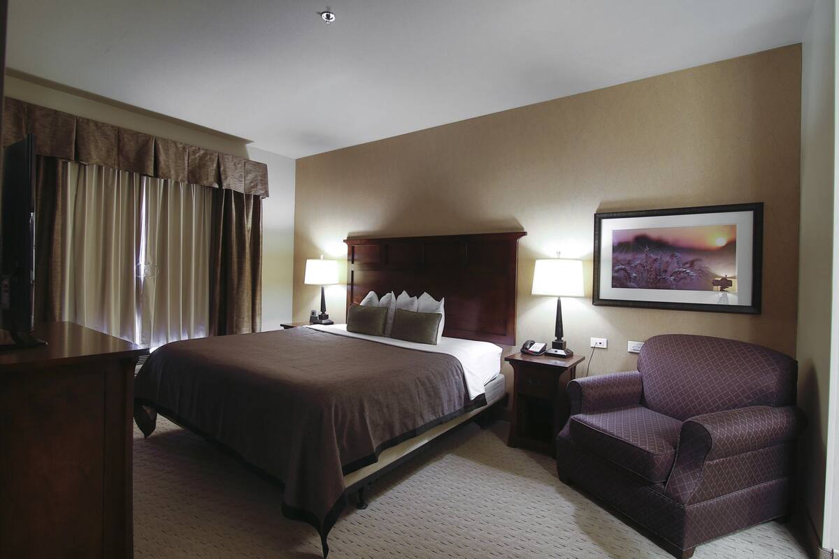 A hotel room with a large bed, a chair, a desk, and a nightstand with lamps.