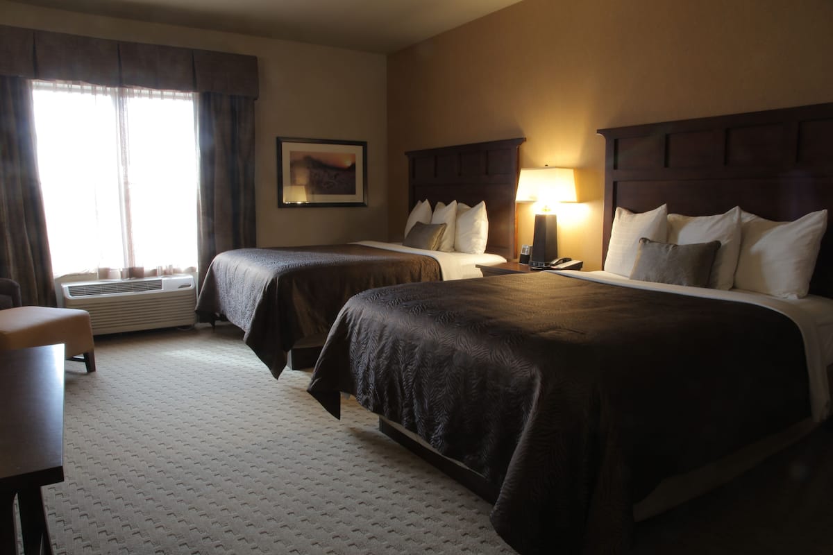 A hotel room with two beds, a desk, a chair, a lamp, and a painting on the wall.