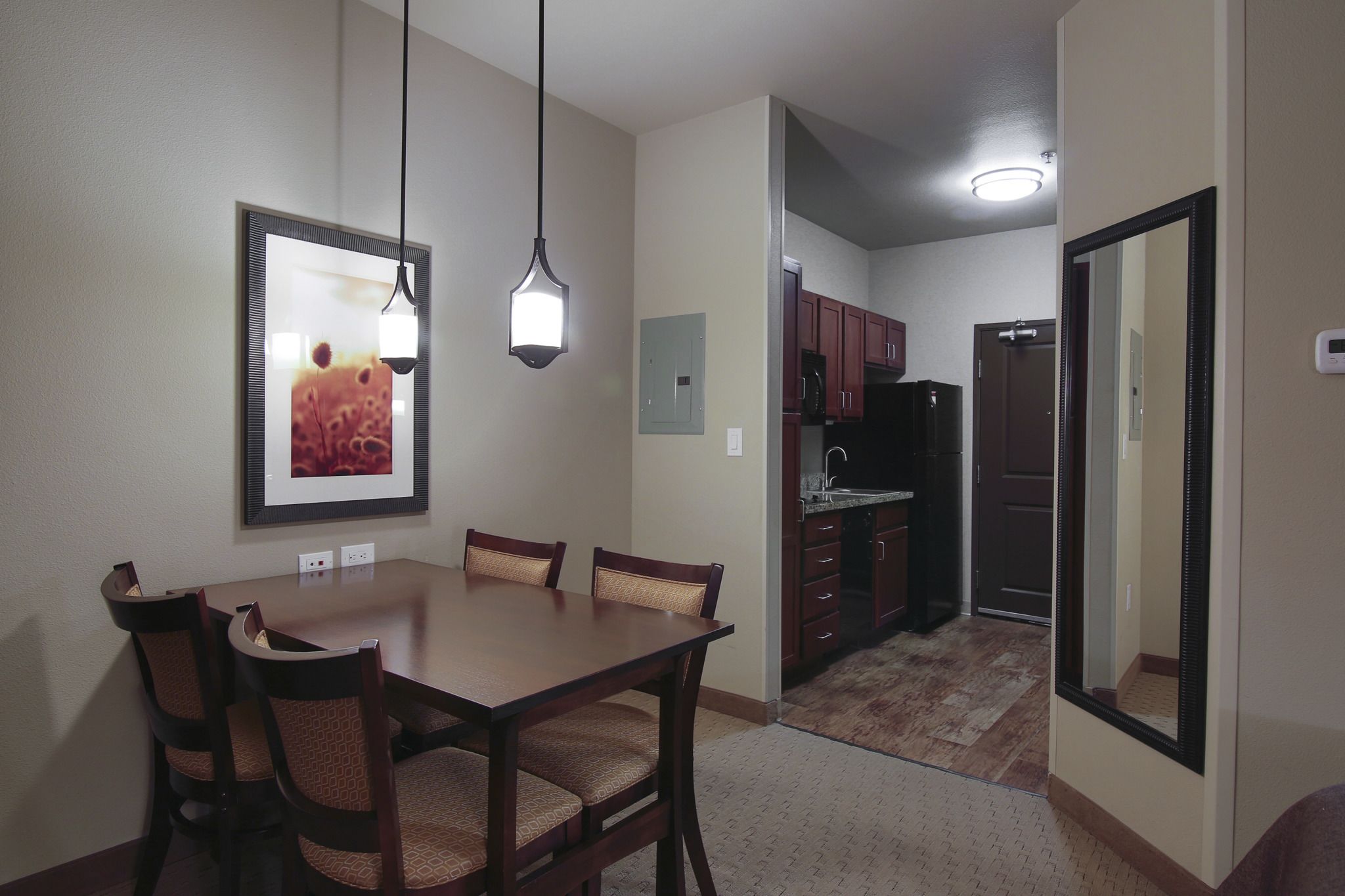 Un comedor con mesa y sillas de madera, una lámpara colgante y un cuadro en la pared.