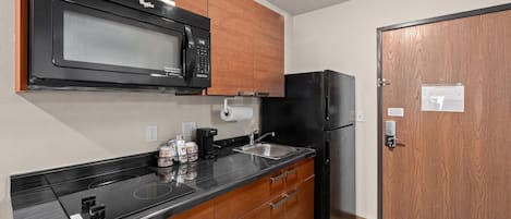 A compact kitchen with a black microwave, a refrigerator, wooden cabinets, a sink, and a coffee maker.