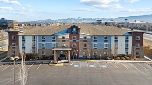 A multi-story hotel with a central entrance, parking lot, and a view of distant mountains. - MainStay Suites Spokane Valley (Spokane Valley)