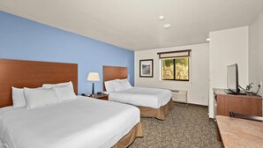 A hotel room with two beds, a desk, a TV, and a window with a view.