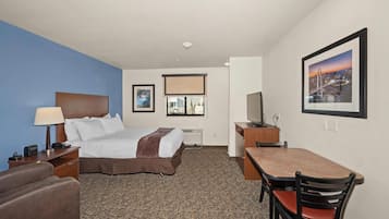 Habitación de hotel con cama, escritorio, silla, lámpara y un cuadro en la pared.