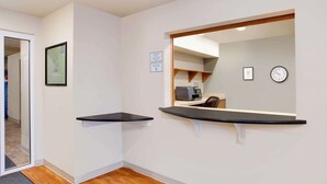 Ein Hotel-Rezeptionsbereich mit einer Rezeption, einer Uhr und einem gerahmten Zertifikat an der Wand.