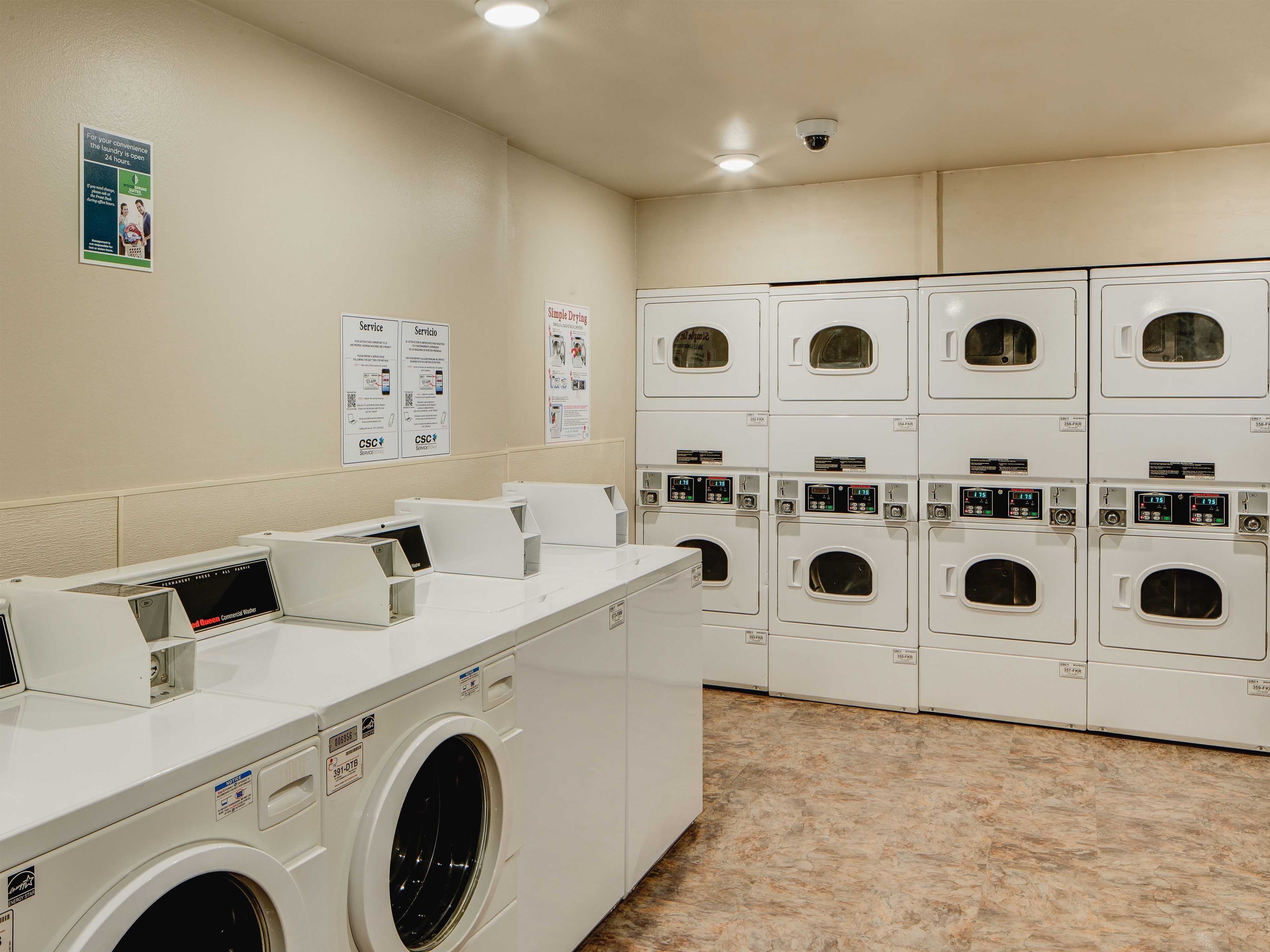 A laundry facility with multiple washing machines and dryers, service posters on the wall, and a control panel for the machines.