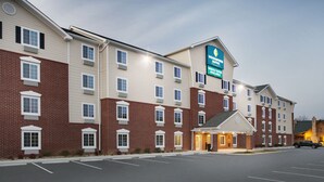 A multi-story hotel with a brick facade, a prominent sign for 'Woodspring Suites', and a parking lot in front. - WoodSpring Suites Fredericksburg (Fredericksburg)