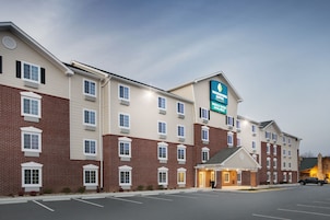 Um hotel de vários andares com fachada de tijolos, uma placa de destaque para 'Woodspring Suites' e um estacionamento na frente.