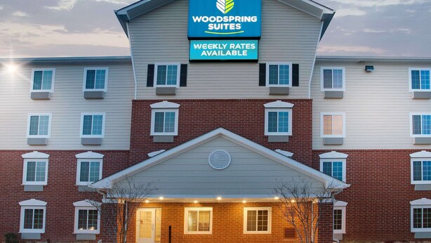 Ein mehrstöckiges Hotel mit einer gut sichtbaren Schautafel für Woodspring Suites, die auf wöchentliche Preise hinweist.