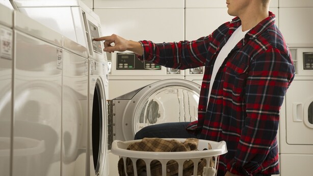A person operating a front-loading washing machine in a laundromat with multiple machines.