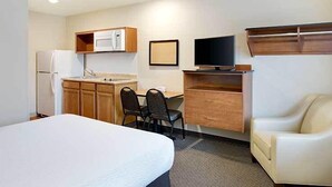 Ein kompaktes Hotelzimmer mit Bett, einer Küchenzeile, einem Schreibtisch mit Stuhl, einem Fernseher und einem Sofa.