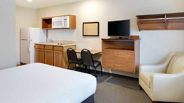 A compact hotel room with a bed, a kitchenette, a desk with a chair, a television, and a sofa. - WoodSpring Suites Fredericksburg (Fredericksburg)