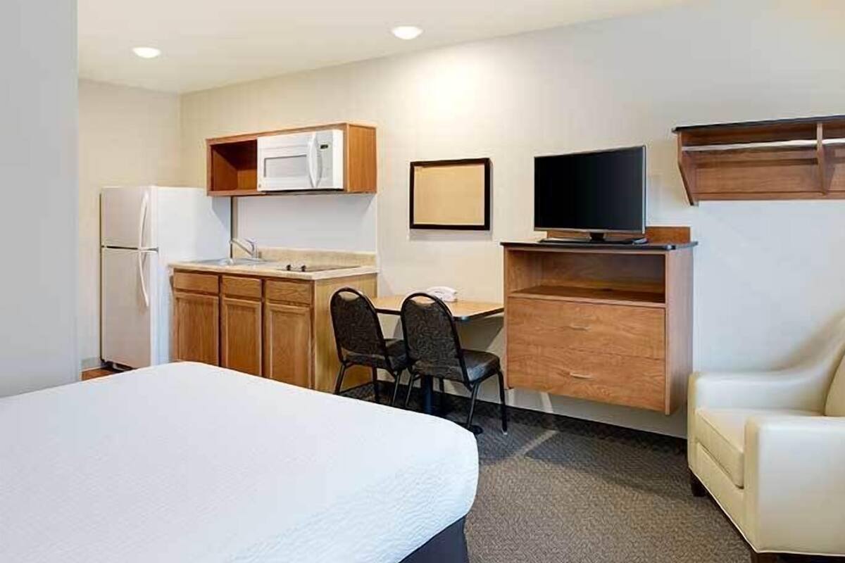 Ein kompaktes Hotelzimmer mit Bett, einer Küchenzeile, einem Schreibtisch mit Stuhl, einem Fernseher und einem Sofa.