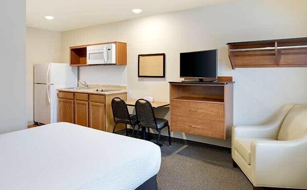 A compact hotel room with a bed, a kitchenette, a desk with a chair, a television, and a sofa. - WoodSpring Suites Fredericksburg (Fredericksburg)
