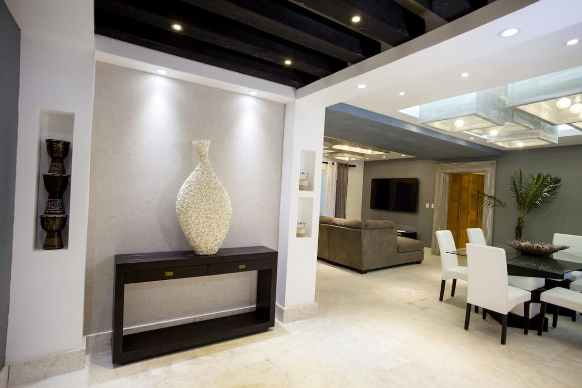 A modern interior with a dining area, a console table with a decorative vase, a sofa, and a television mounted on the wall.
