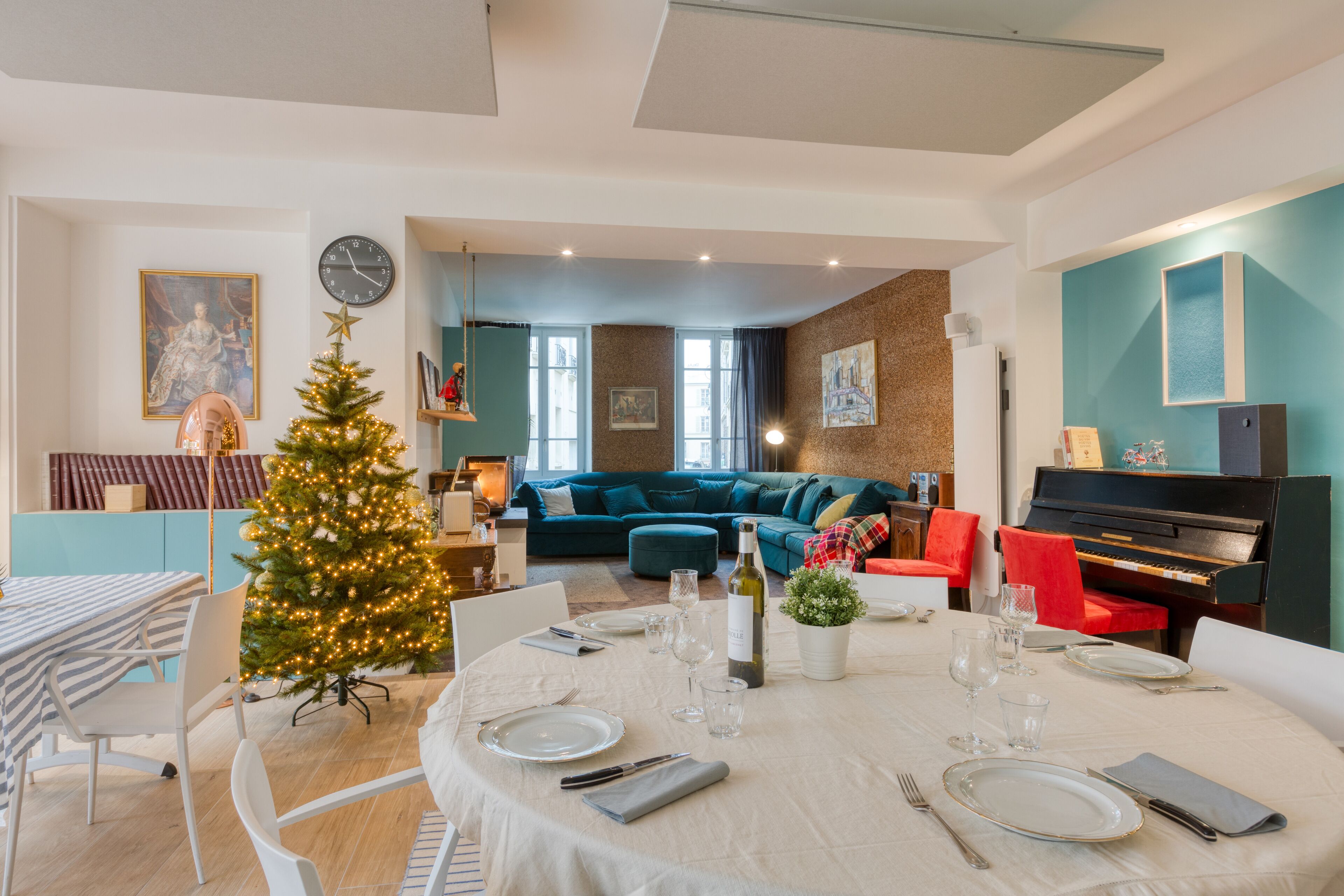 A dining area with a Christmas tree, a piano, and a teal-colored sofa in the background.