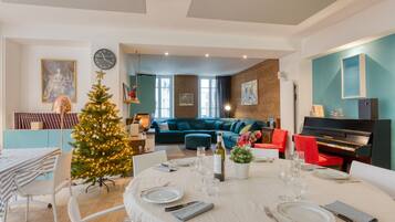 A dining area with a Christmas tree, a piano, and a teal-colored sofa in the background.