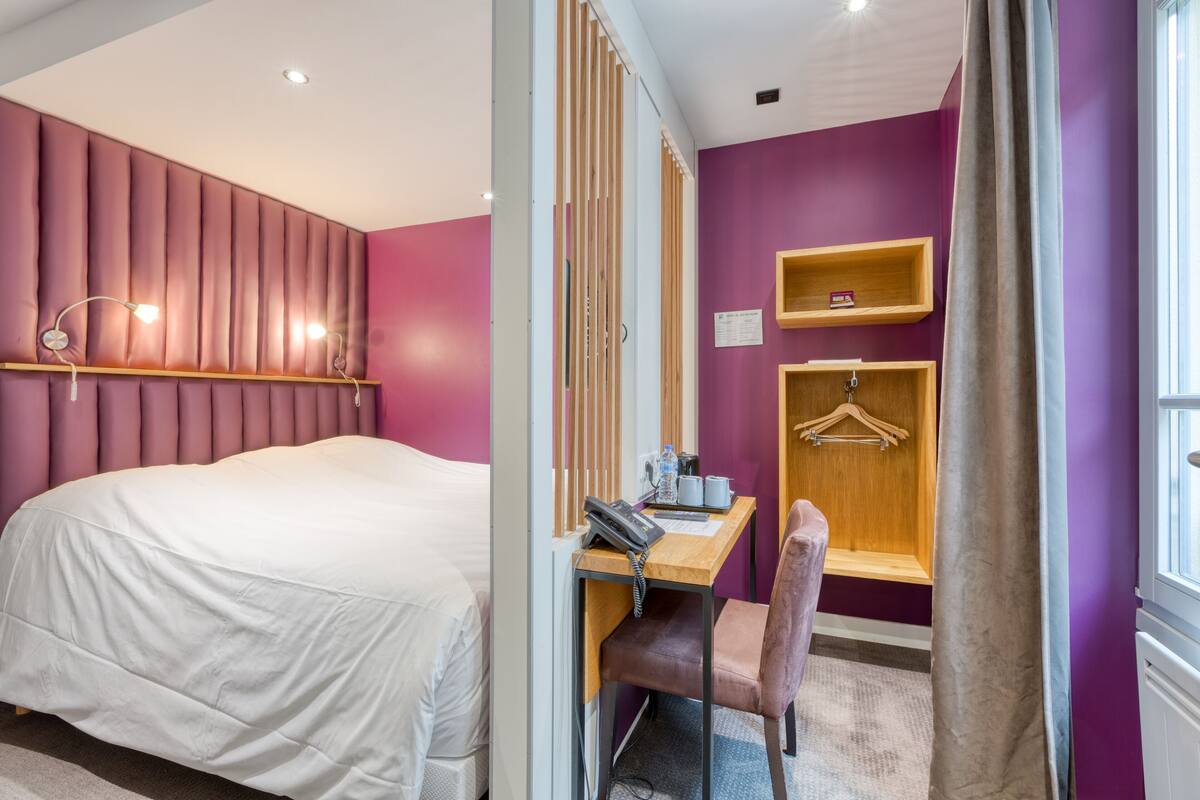 Une chambre d’hôtel comprenant un lit, un bureau avec une chaise, un téléphone et une petite étagère.