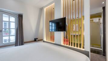 Een hotelkamer met een groot bed, een aan de muur bevestigde televisie en een badkamer zichtbaar door een raam.