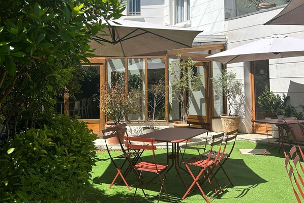Une terrasse extérieure avec une table et des chaises, entourée de plantes en pot et protégée par une structure en verre.