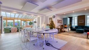 Een ruime woonkamer met een grote eettafel, groene banken en een kerstboom.