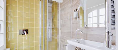 A modern bathroom with a yellow tiled wall, a glass shower enclosure, a white sink, and a toilet.