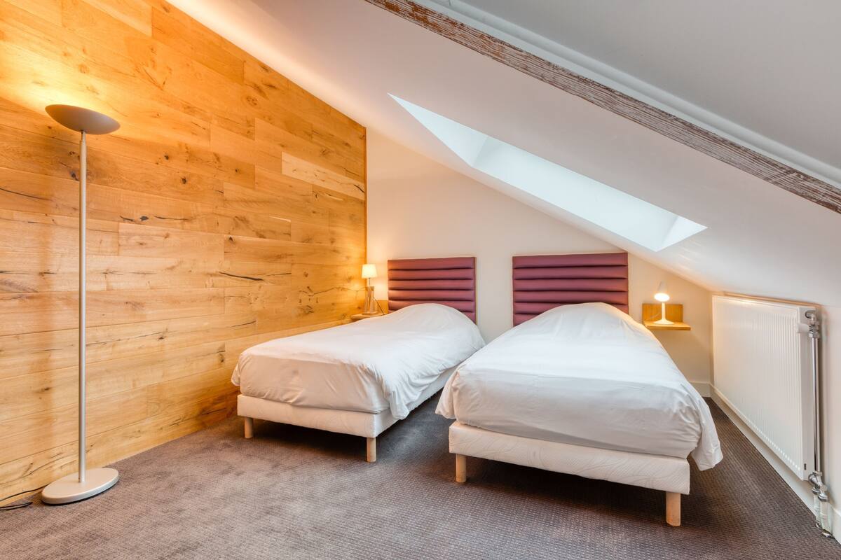 Ein Zimmer mit zwei Betten, einer Holzwand, einer Stehlampe und einem Oberlicht.