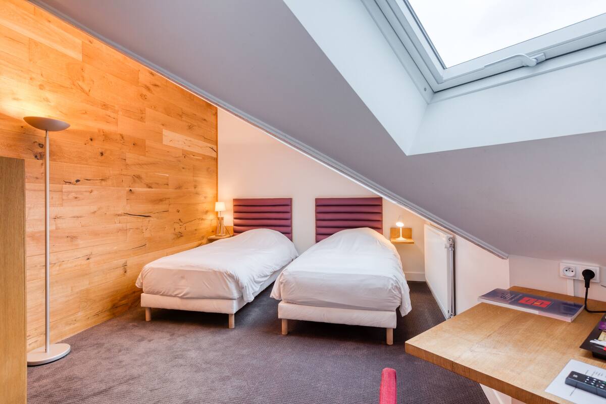 Ein Zimmer mit zwei Betten, einem Schreibtisch, einer Lampe und einem Fenster.