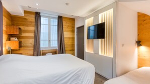 Een moderne hotelkamer met twee bedden, een televisie bevestigd aan een houten wand, een raam met gordijnen en een accentwand van hout.