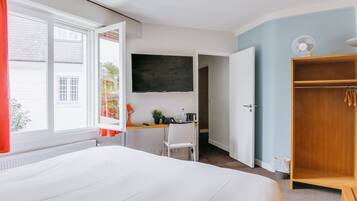 Habitación de hotel con cama, escritorio con silla, televisor, armario y ventana con cortinas.