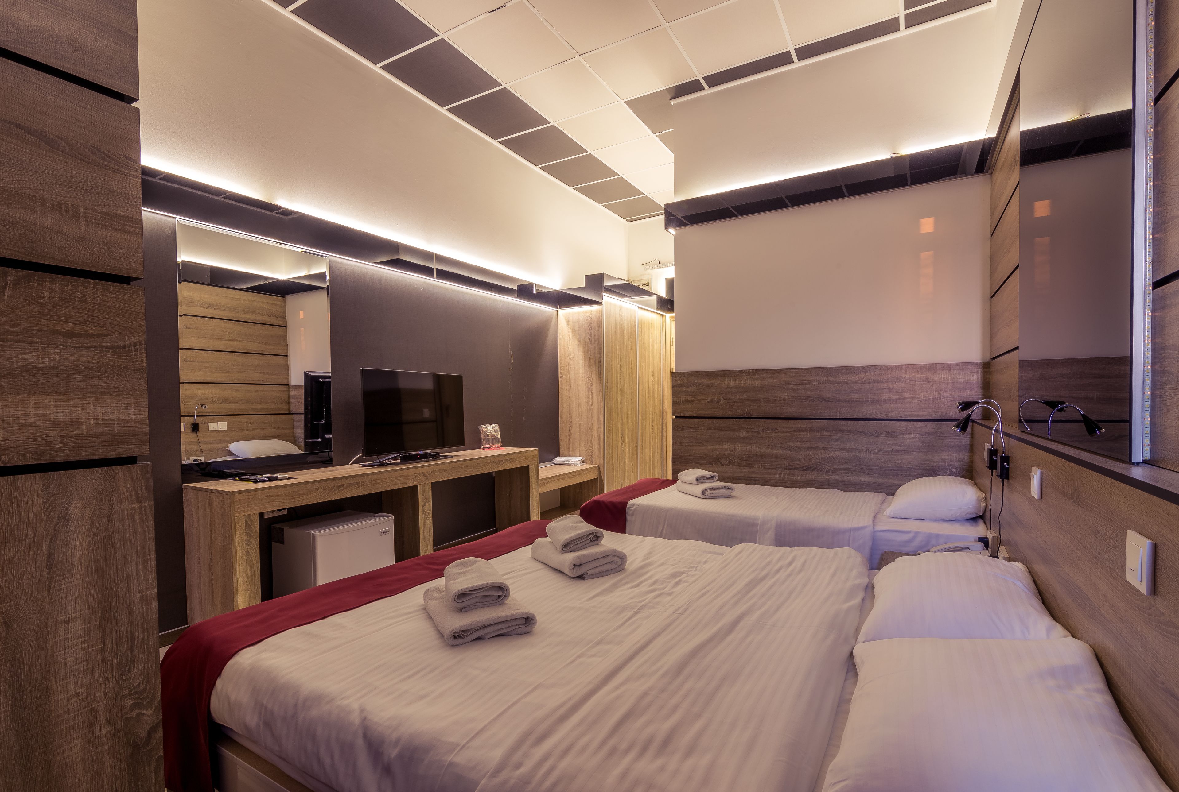 A hotel room with two beds, a desk with a TV, and a mirror.