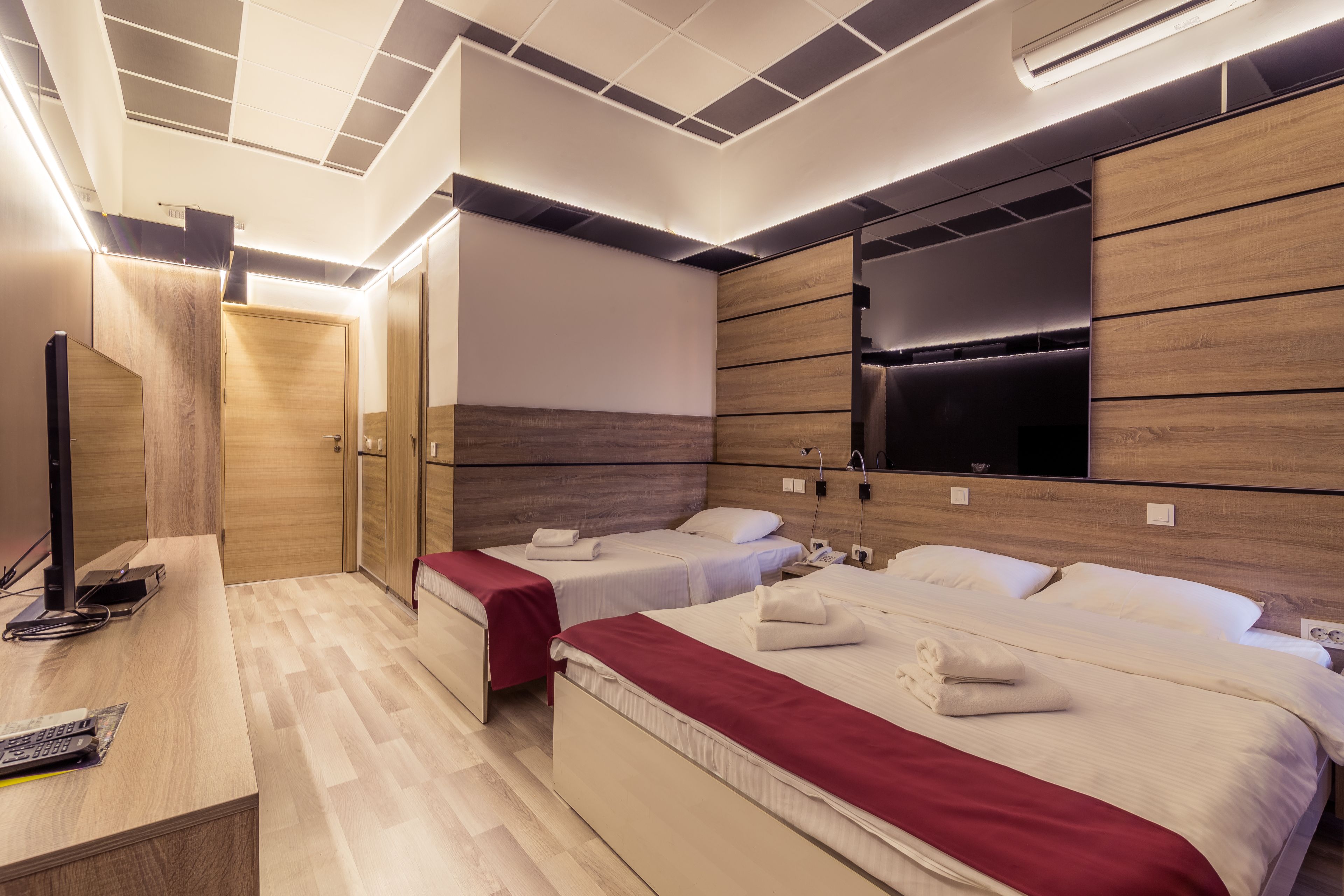 A hotel room with two beds, a desk with a computer, and a flat-screen TV mounted on the wall.