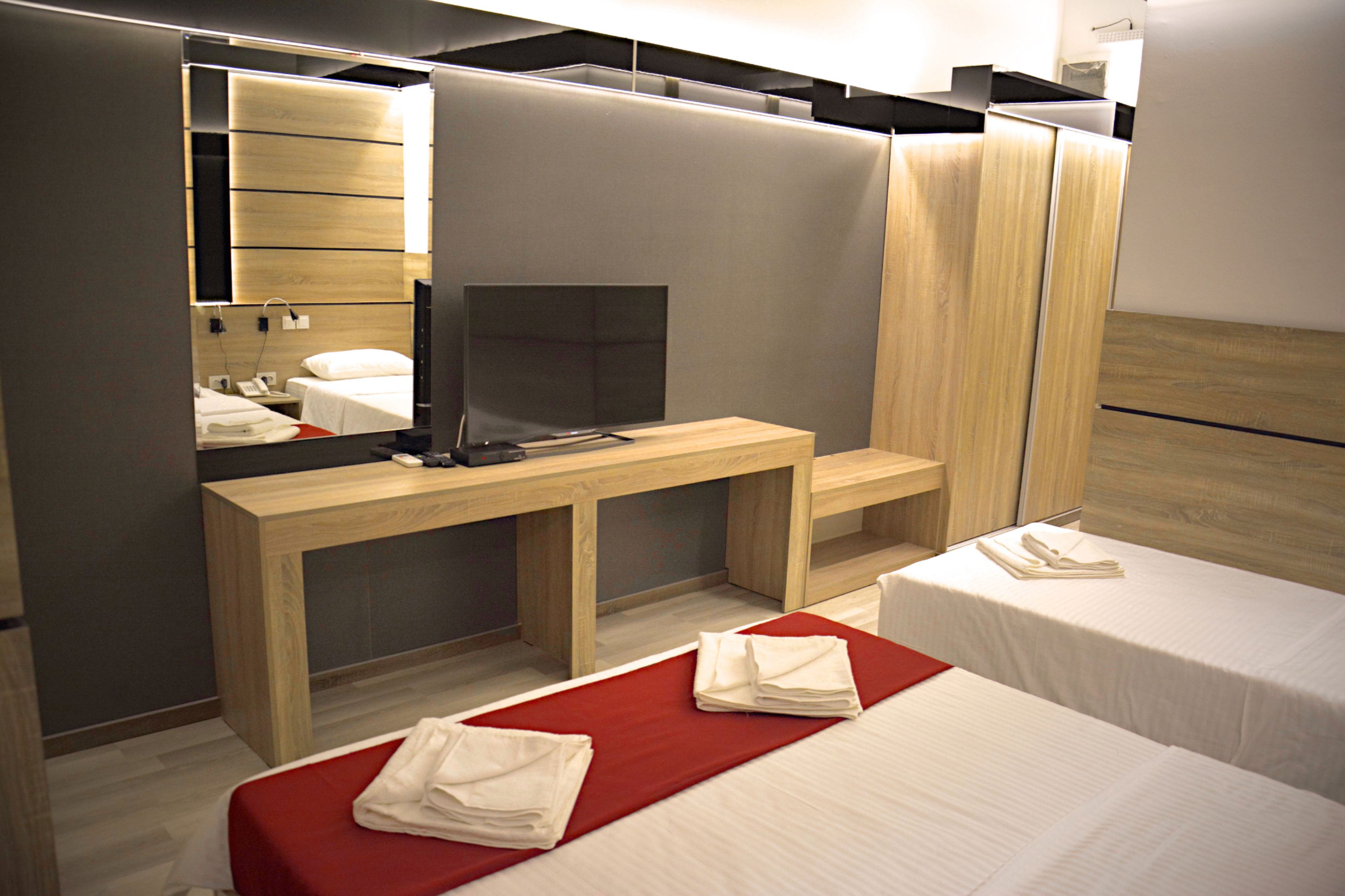 Habitación de hotel con un escritorio de madera, televisor, dos camas y un espejo.